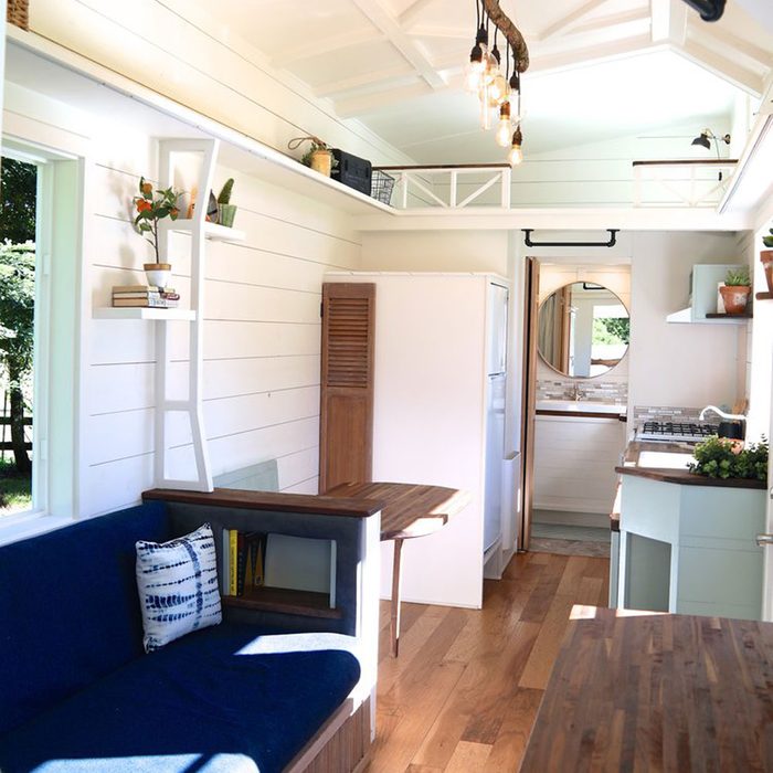 A cozy, modern kitchenette with white walls, wooden accents, a blue couch, and a circular mirror reflects a bright, inviting atmosphere.