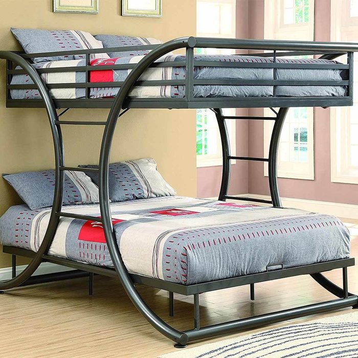 A bunk bed with a curved metal frame displays a lower double bed and an upper single bed, set against a light-colored wall with windows.