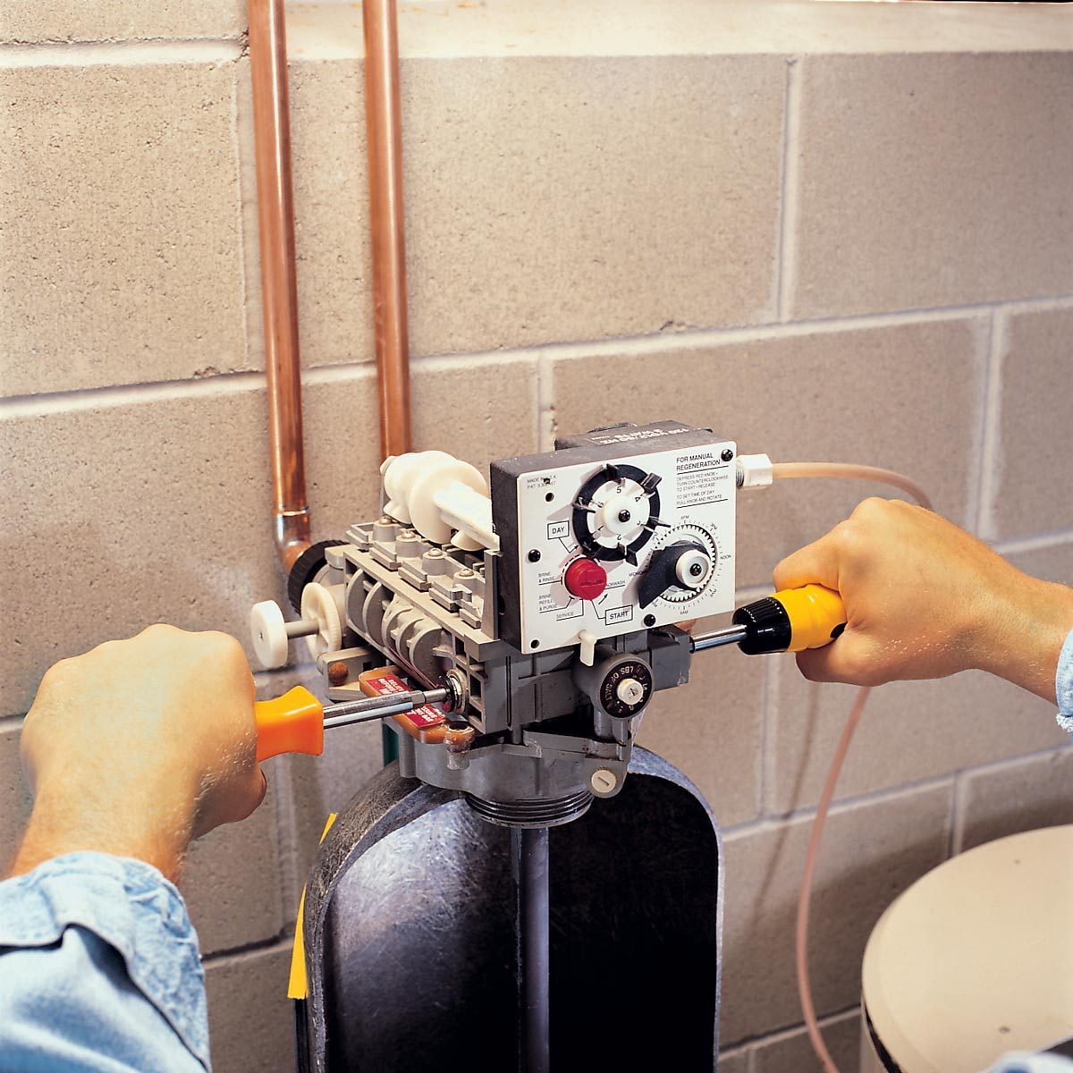 A person is adjusting a valve with a wrench on a connected device, located in a basement with concrete walls.