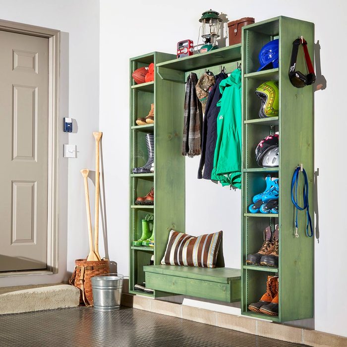 A green storage unit holds clothes, shoes, and equipment, with a bench below. It’s placed near a door, with paddles and a bucket nearby.