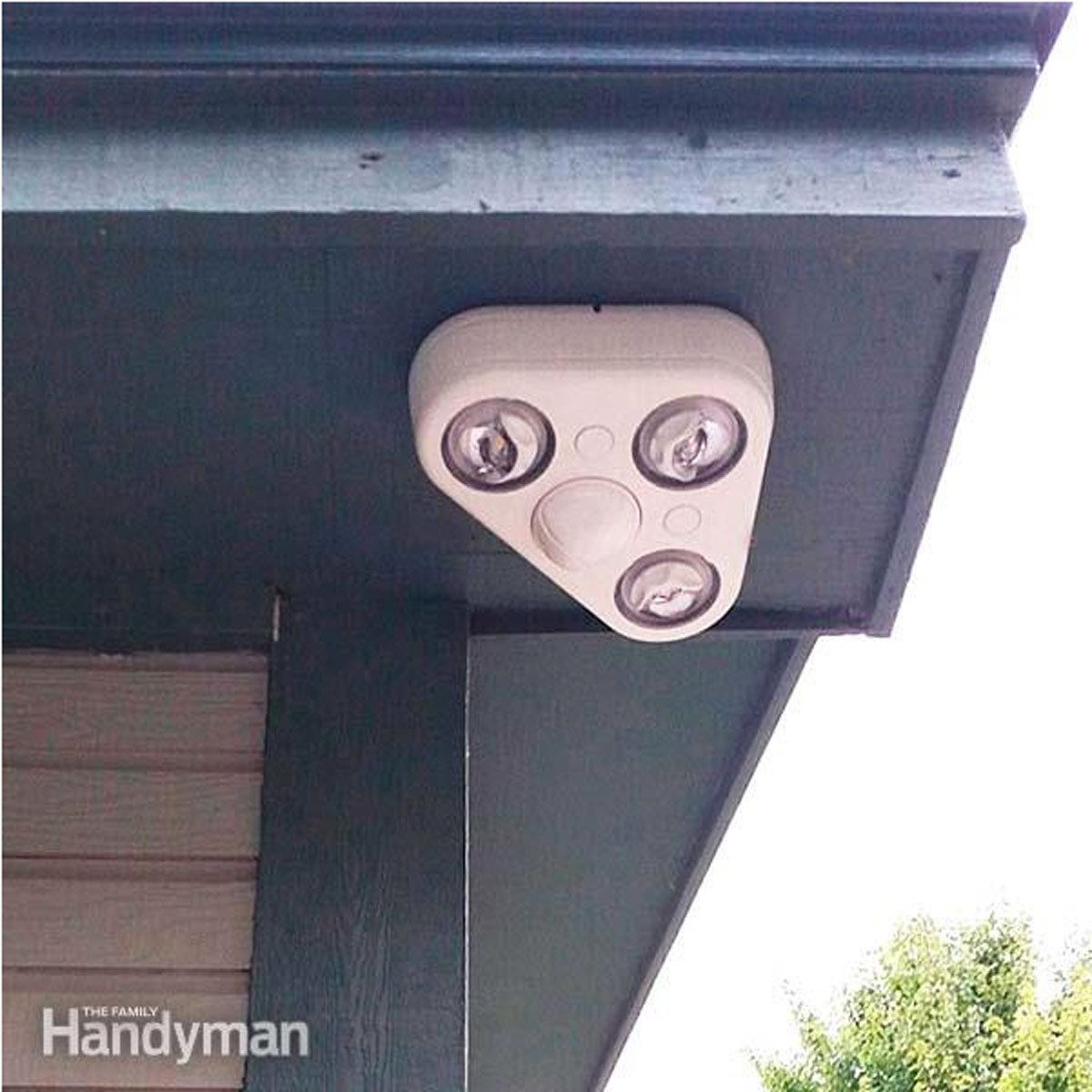 A triangular motion sensor light is mounted under an eave, illuminating the surrounding outdoor area, featuring three bulbs and a central sensor.