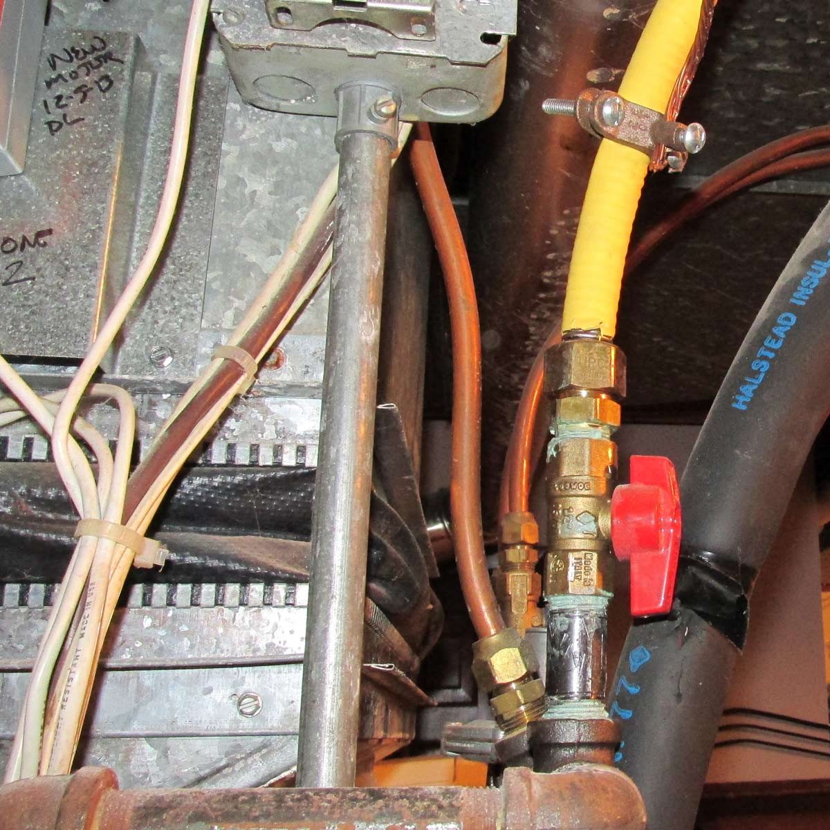 A series of interconnected pipes and valves exhibit various materials and colors, mounted on a metallic surface in a utility area, suggesting plumbing or heating installation.