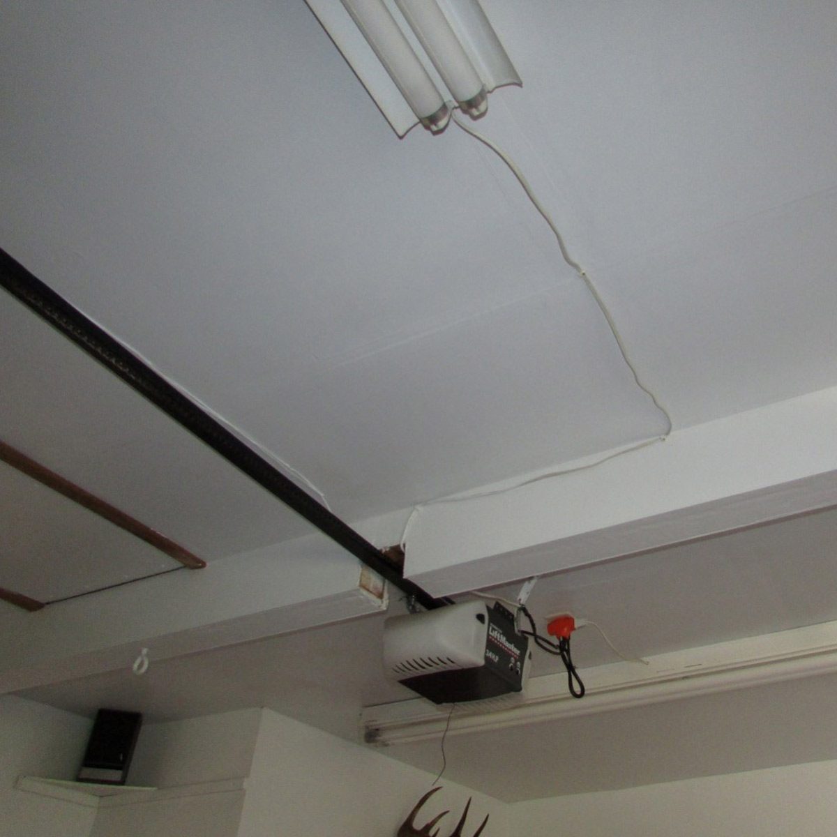 A ceiling-mounted unit with lights and a heater is installed near a wall, surrounded by exposed wires and a speaker on a shelf.