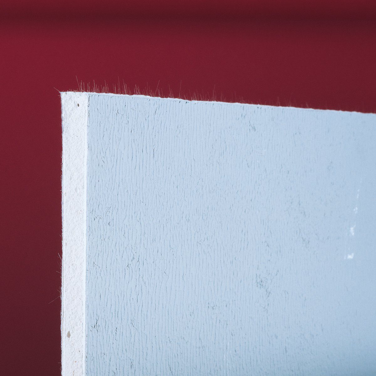 A light blue wall panel stands against a deep red background, highlighting its textured surface and fine edges.