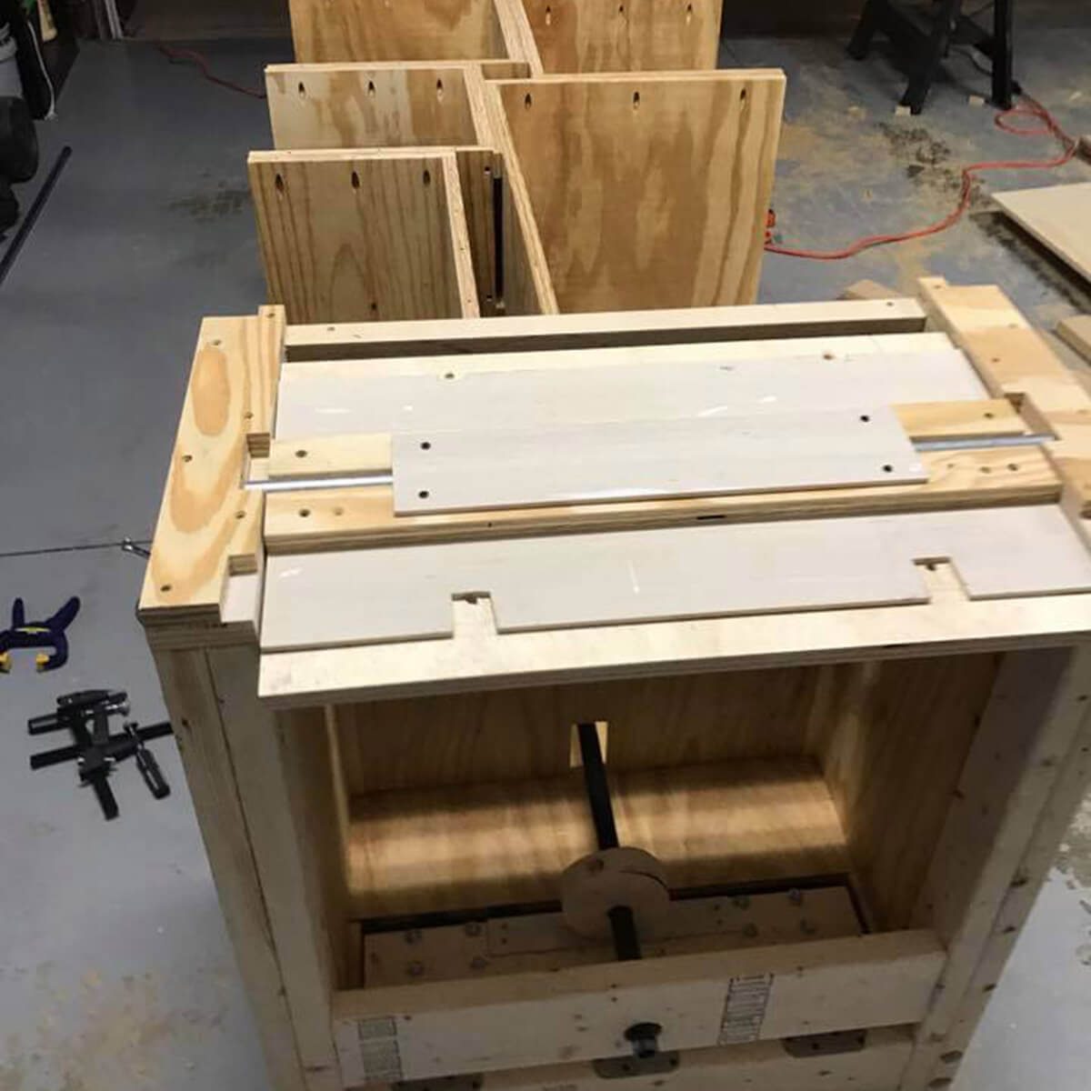 A wooden structure with various components is being assembled in a workshop. Tools and materials are scattered across the floor, indicating an active construction process.