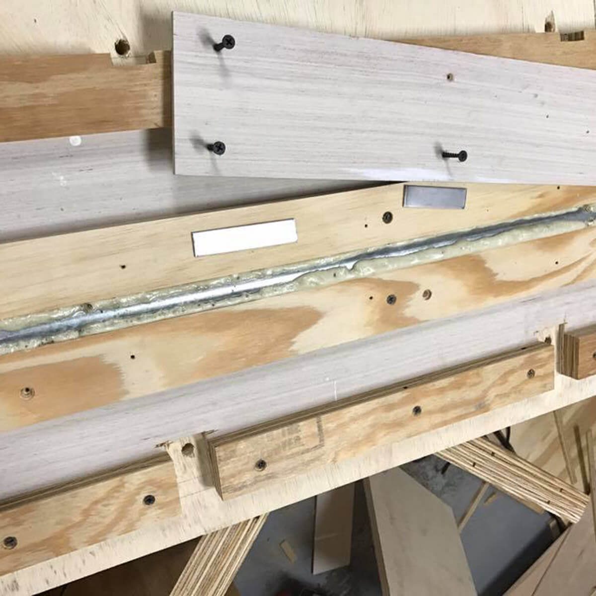 A variety of wood pieces are arranged on a surface, partially attached with screws. A strip of sealant runs along the center.