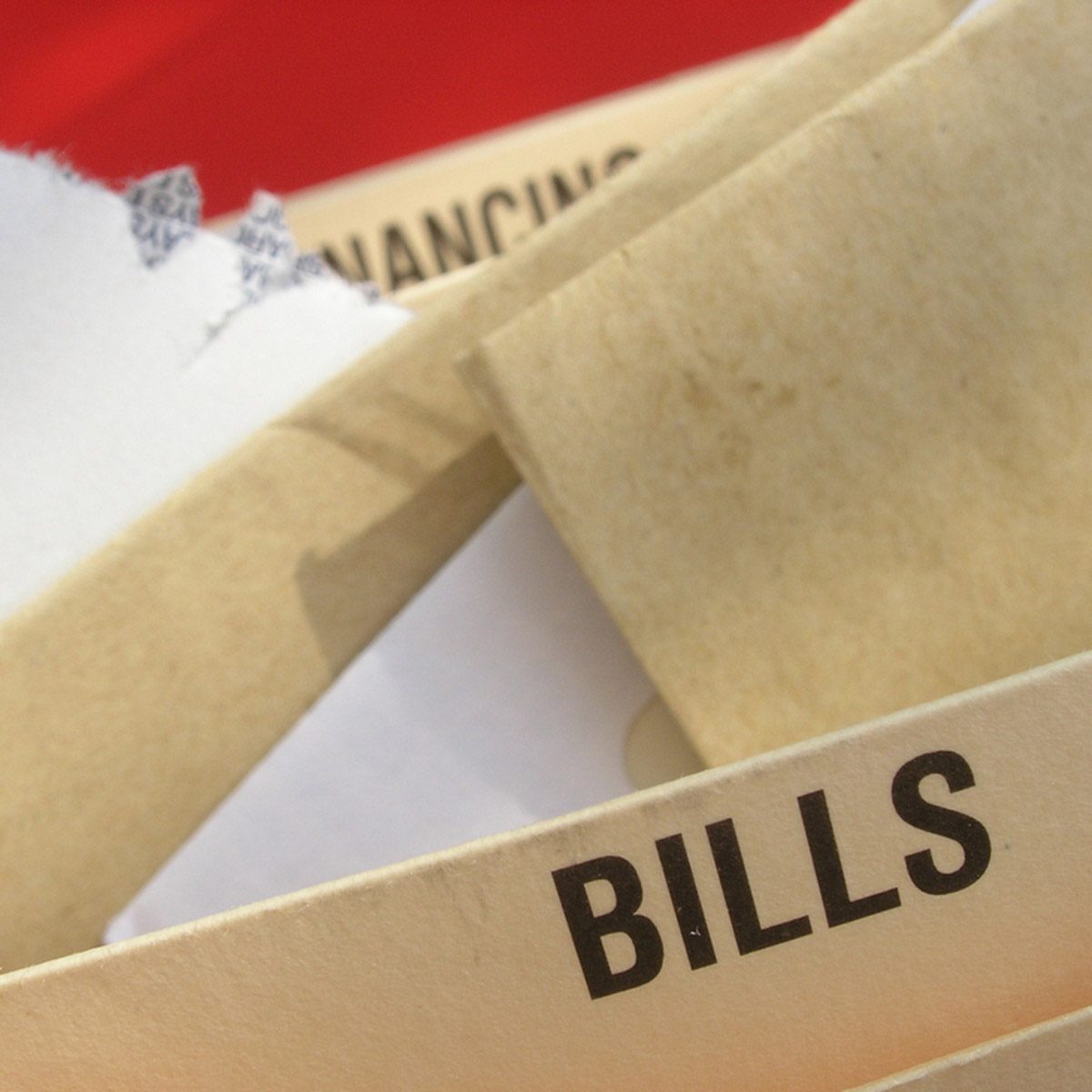 Folders labeled "BILLS" and "FINANCING" are stacked, with a torn edge revealing white paper. The surroundings are blurred, hinting at indoor organization.