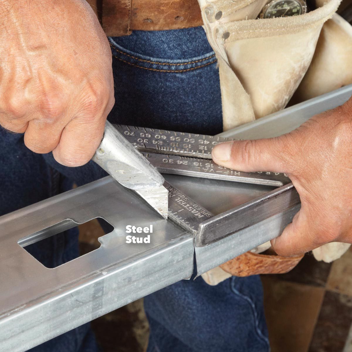 A hand uses a utility knife to cut a steel stud while another hand holds a square measuring tool, set against a casual indoor workspace.