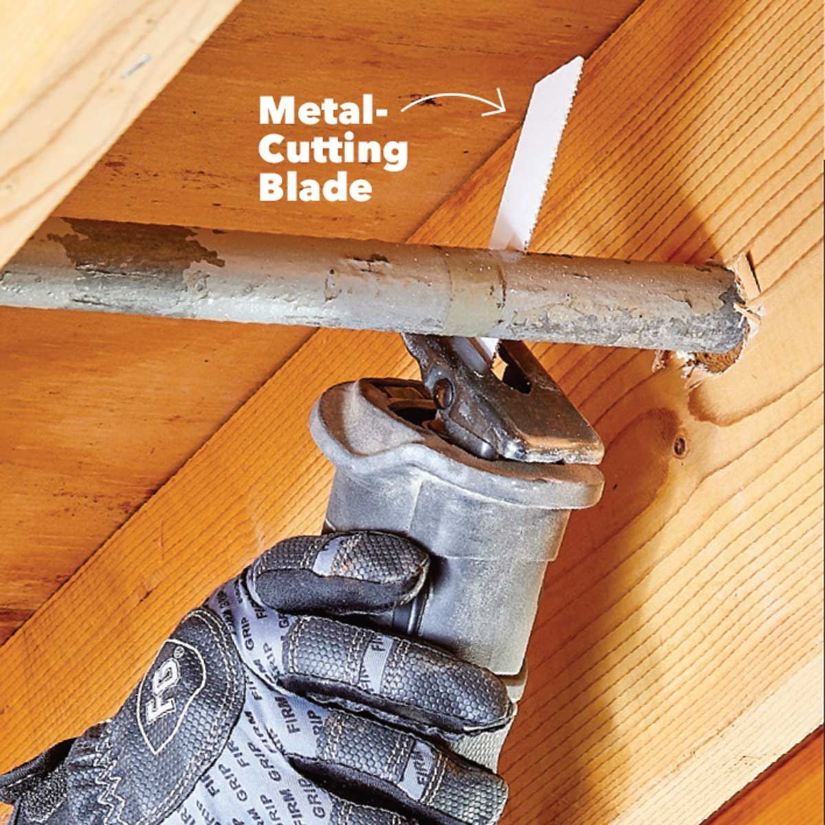 A hand holds a power tool with a metal-cutting blade, cutting through a metal pipe located within a wooden environment.