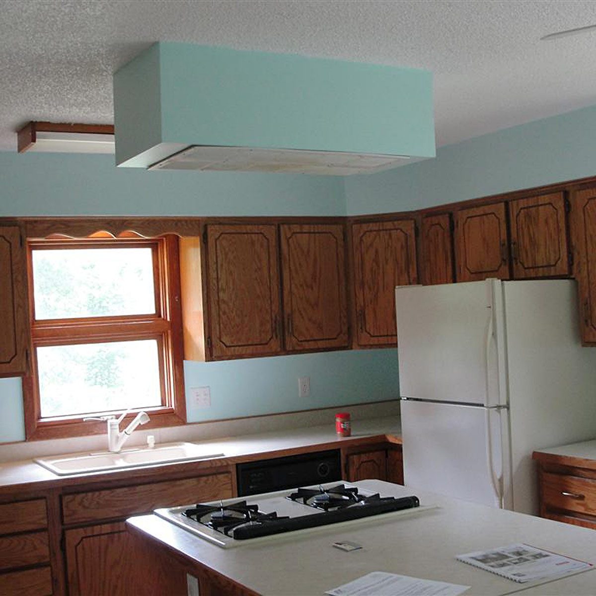 A kitchen features wooden cabinets, a sink with a faucet, and a countertop with a gas stove, illuminated by natural light from a nearby window.