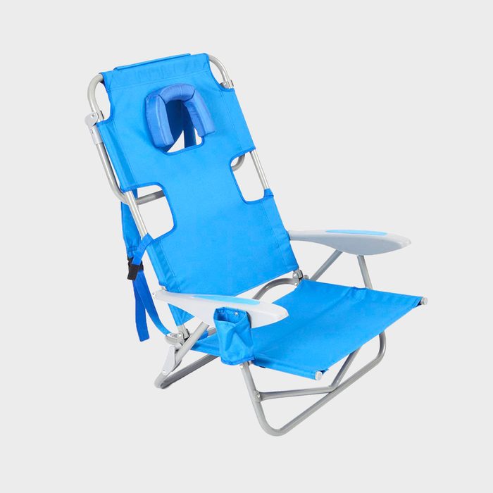A blue folding beach chair is positioned upright, featuring a supportive headrest, armrests, and a cup holder, suitable for outdoor relaxation.