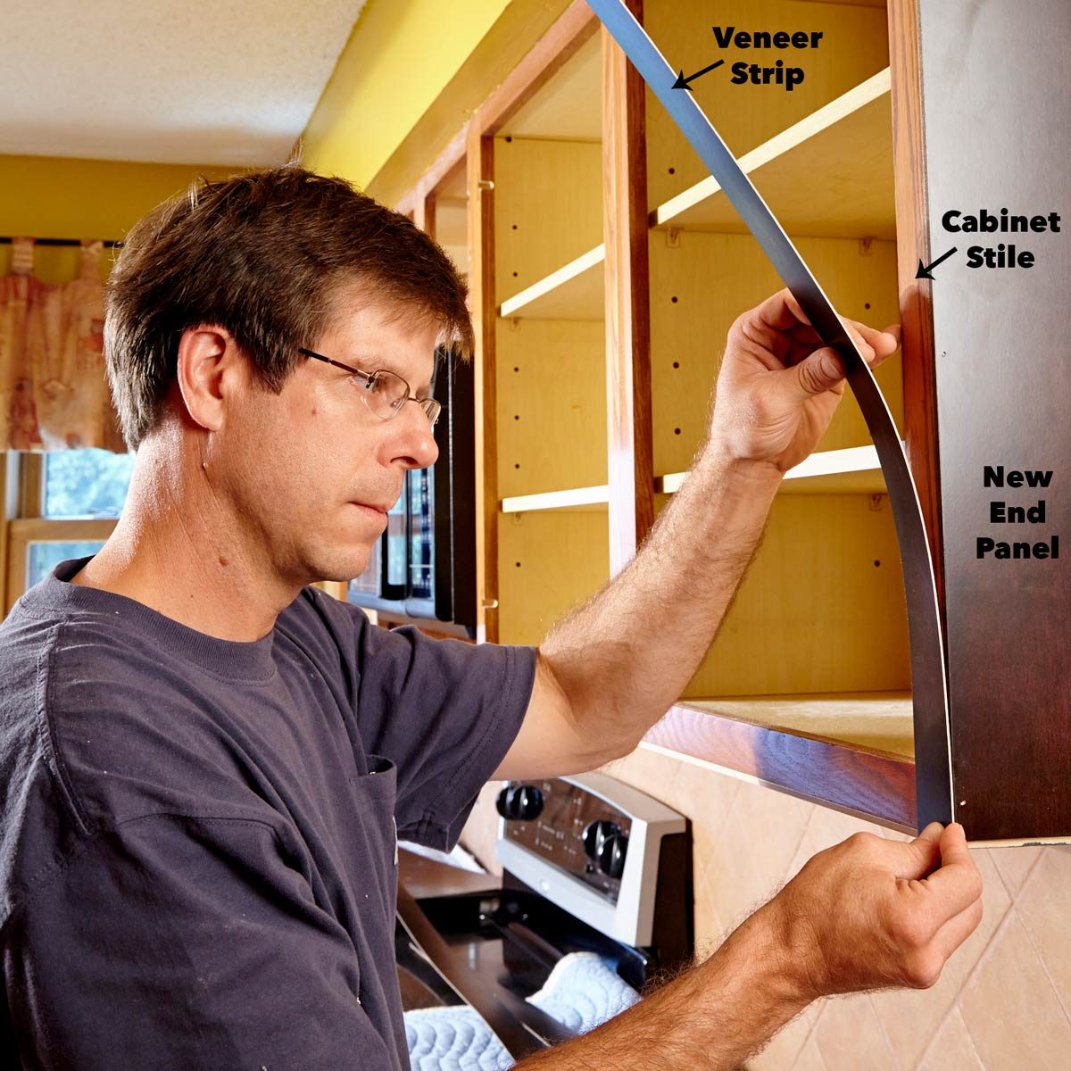 A man attaches a veneer strip to a kitchen cabinet's end panel, focusing intently amid a home renovation setting with appliances nearby.