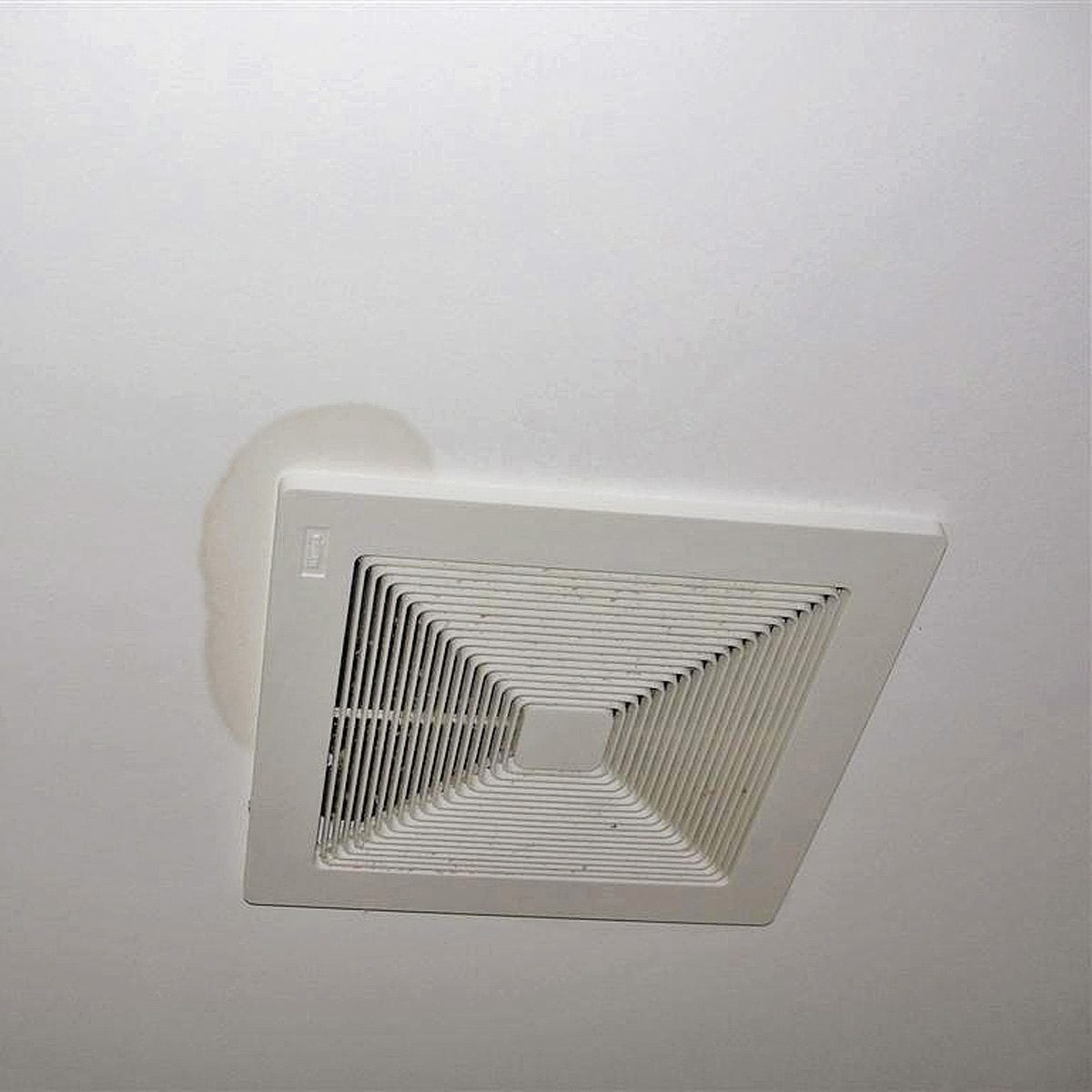 A ceiling vent is mounted on a white surface while a brownish stain spreads around it, indicating possible water damage in the room.