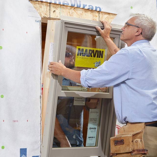 Two men placing a window into place | Construction Pro Tips