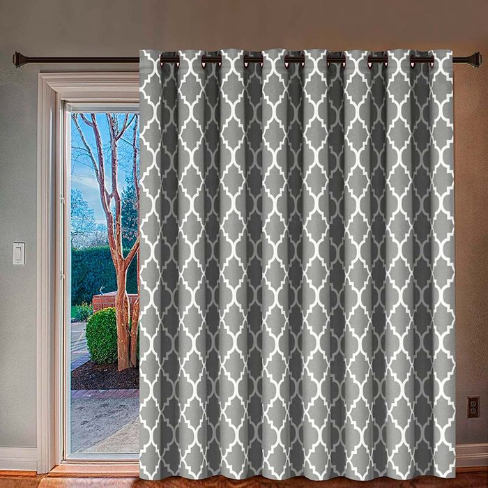 A patterned curtain hangs in a doorway, partially obscuring a view of trees and shrubbery outside in a well-lit room.
