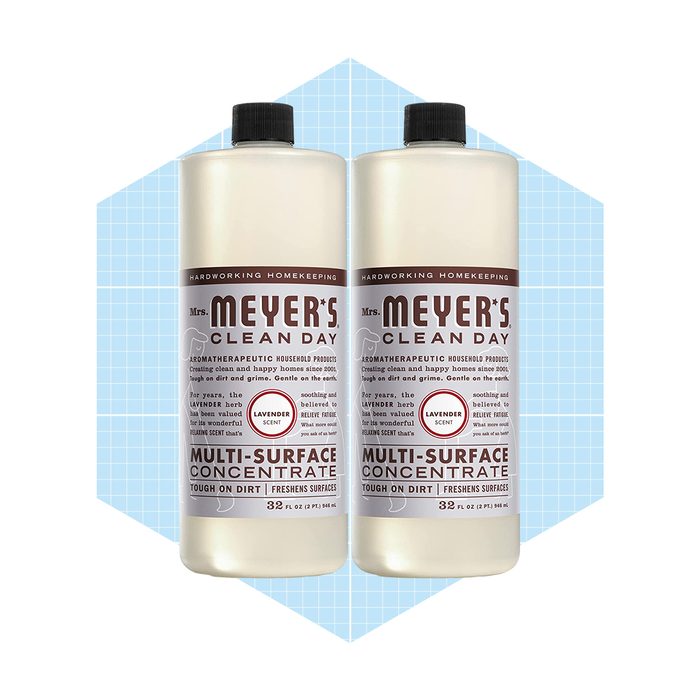 Two bottles of Mrs. Meyer's lavender-scented multi-surface cleaner stand upright, labeled for cleaning effectiveness, set against a light blue geometric background.