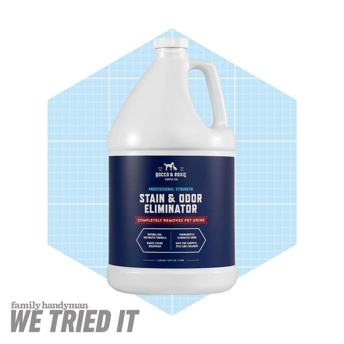 A large bottle of stain and odor eliminator is displayed against a blue grid background, indicating its use for removing pet urine stains.