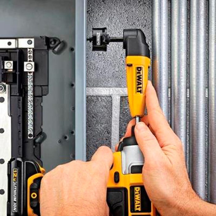 A hand holds a yellow and black DEWALT drill, attaching equipment inside a gray metal enclosure, surrounded by metal pipes and electrical components.