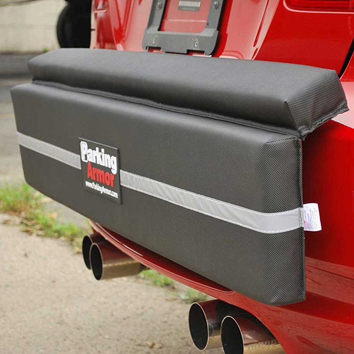 A black parking bumper cushion is attached to a red vehicle's rear, designed to absorb impacts while parked, set against a pavement background.