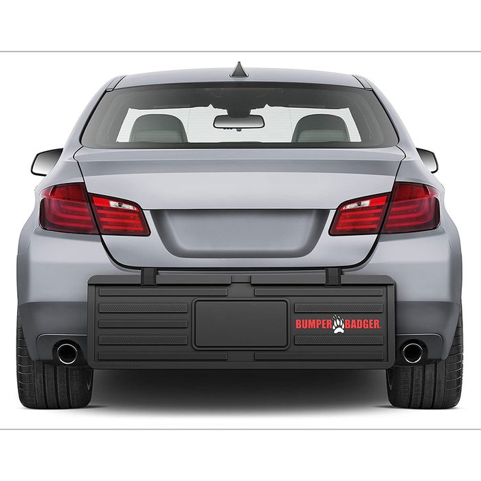 A gray car with a protective bumper guard attached is parked. The guard displays the text 