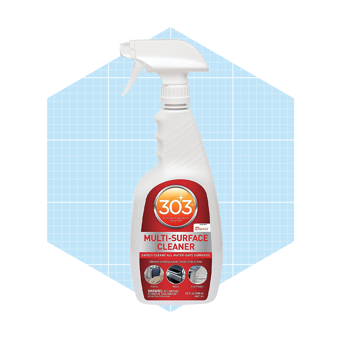 A spray bottle of multi-surface cleaner is positioned against a light blue hexagonal background, indicating its purpose for cleaning various surfaces safely.