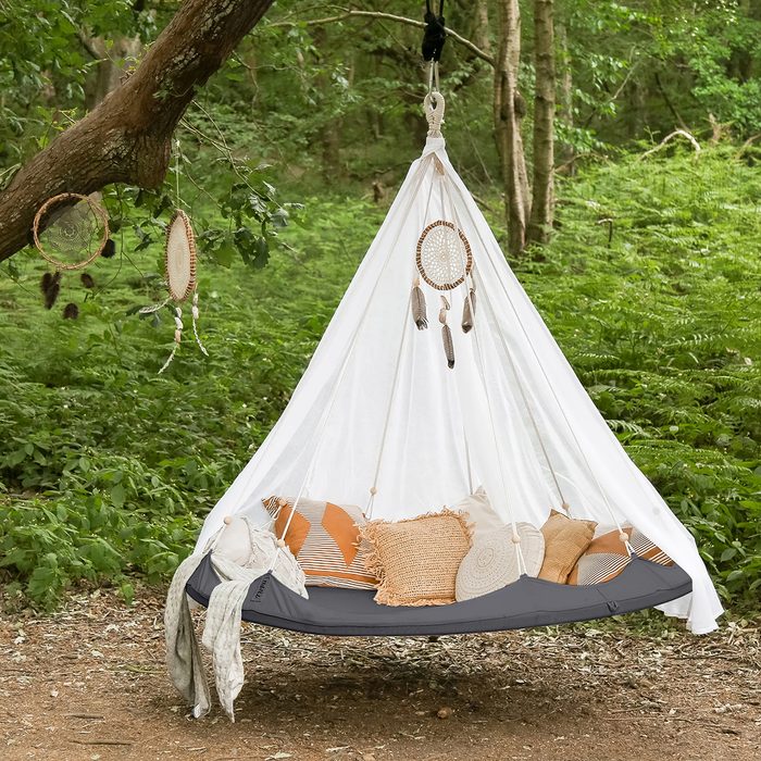 A hanging hammock with soft pillows sways gently among trees, surrounded by lush greenery, while dreamcatchers dangle nearby.