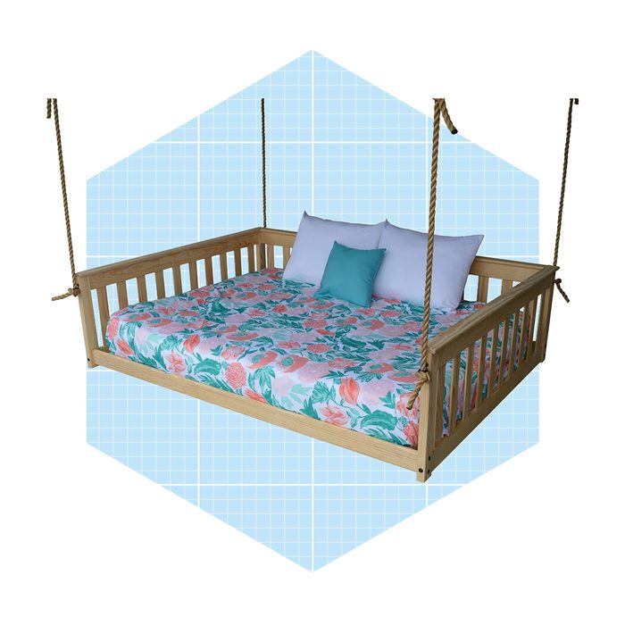 A wooden swing bed with a floral-patterned mattress and decorative pillows gently sways, set against a light blue grid background.