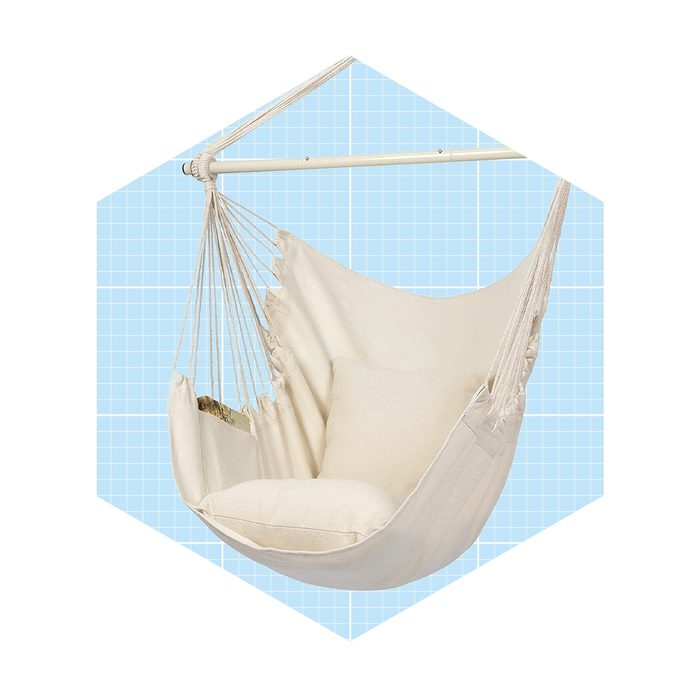 A suspended, beige hammock with a cushion swings gently against a light blue grid background, inviting relaxation and comfort in a cozy setting.