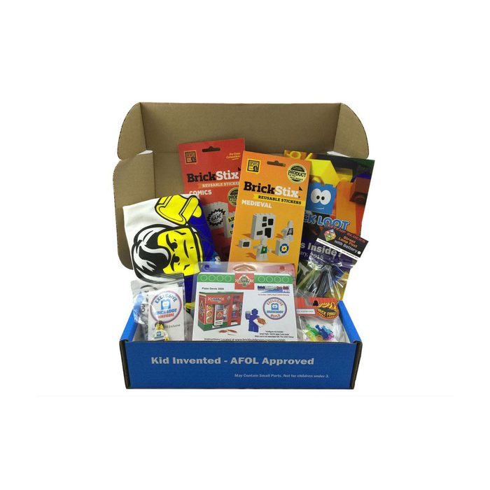 A blue box containing various items including stickers, a T-shirt, and toys is open, revealing colorful packaging and instructional cards in a plain background.