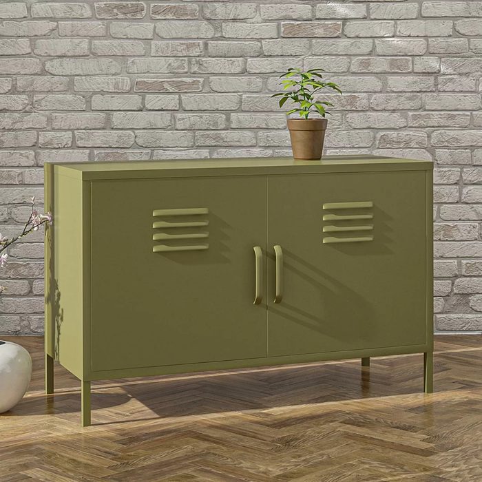 A green cabinet with slatted doors holds a potted plant on top, set against a textured brick wall and wooden floor.