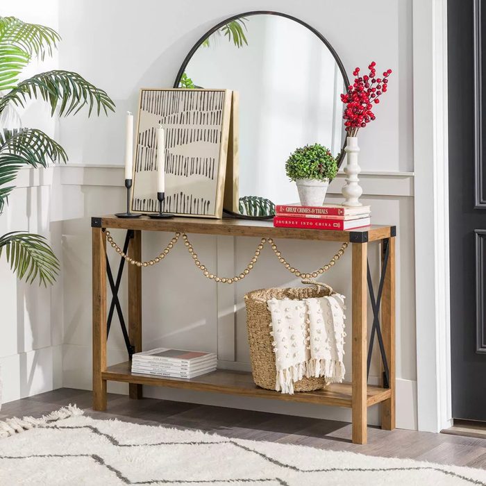 A wooden console table displays decorative items, including a mirror, plants, and books, next to a black door, surrounded by light walls and a soft rug.