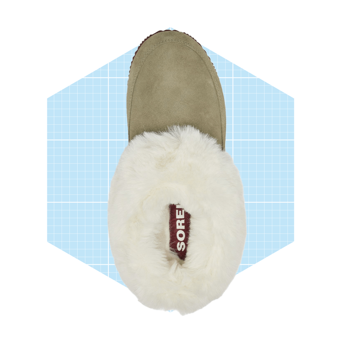 A fuzzy, olive-green slipper rests on a light blue grid background, showcasing its soft collar and brand label inside.