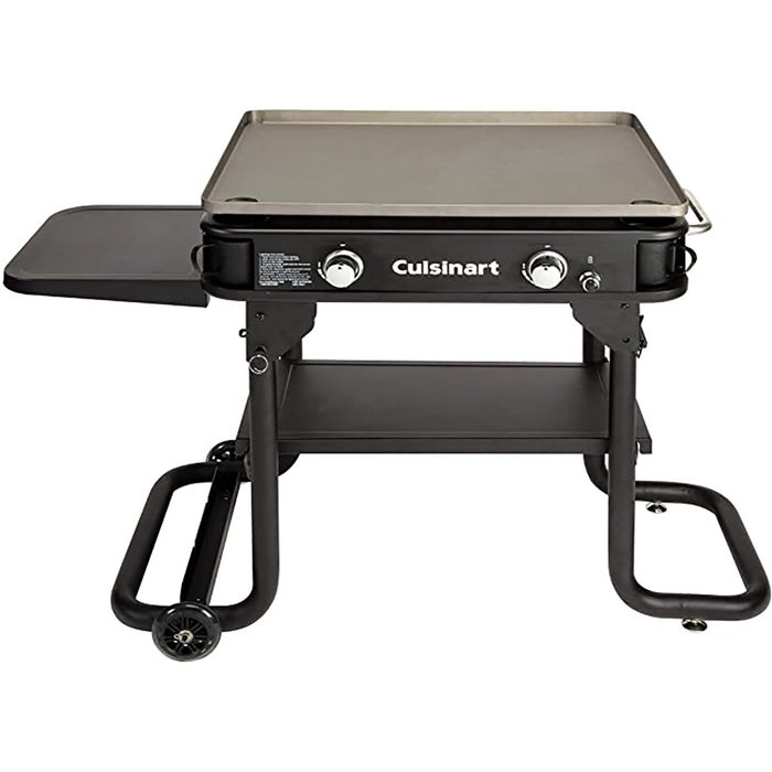 A black outdoor griddle sits on a wheeled cart, featuring a large cooking surface and control knobs, designed for grilling in various outdoor contexts.