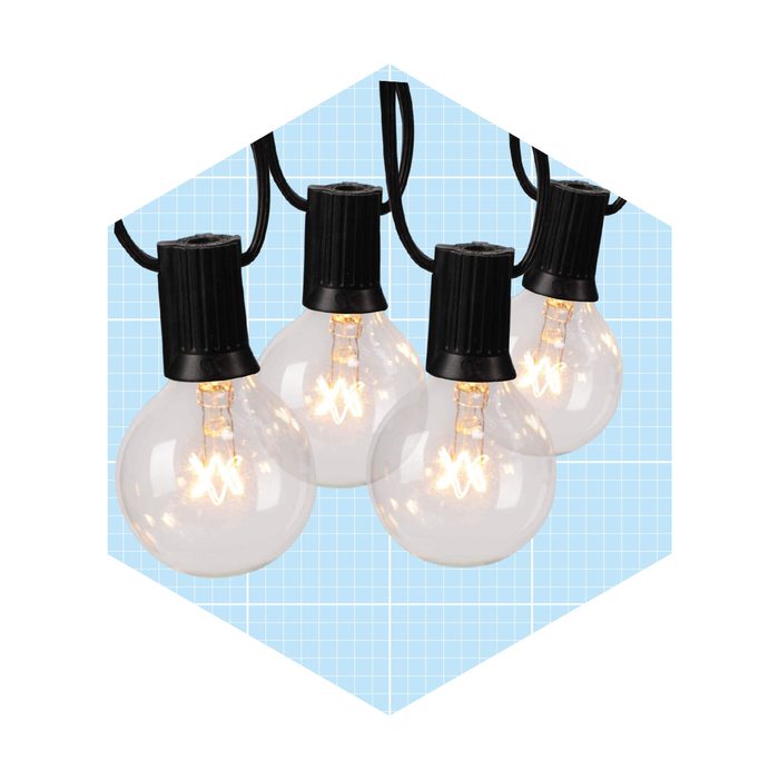 Four decorative light bulbs hang from a black cord, illuminating softly against a light blue grid background. The bulbs are clear with warm glowing filaments inside.