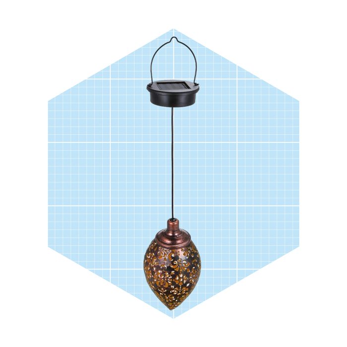 A decorative solar pendant light hangs from a black wire, illuminating a patterned metallic shade against a light blue, grid-patterned background.