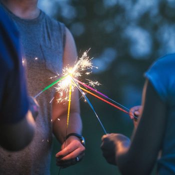 Sparklers held by individuals produce bright sparks while they gather together outdoors during twilight, creating a festive, cheerful atmosphere.