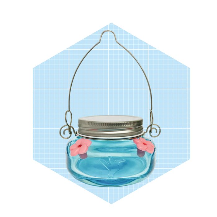 A decorative glass jar with pink flowers on the sides is hanging from a wire handle against a light blue grid background.
