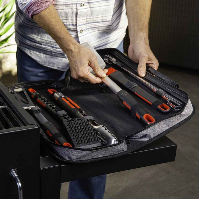 A person is removing a tool from a zipped case filled with various cooking utensils, set on a flat surface in an outdoor environment.