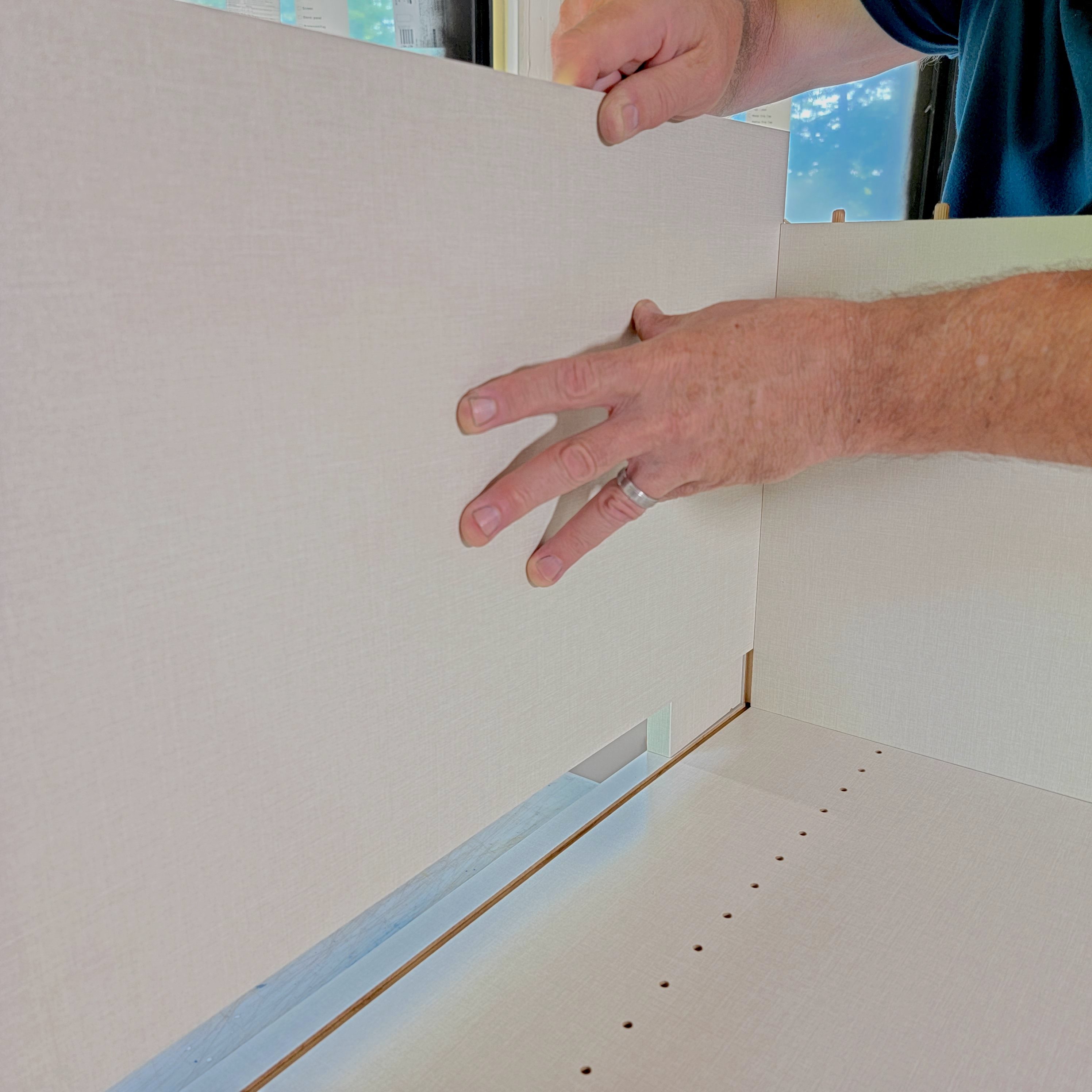 A hand positions a light-colored panel into place, aligning it with a nearby structure, in a well-lit indoor environment.