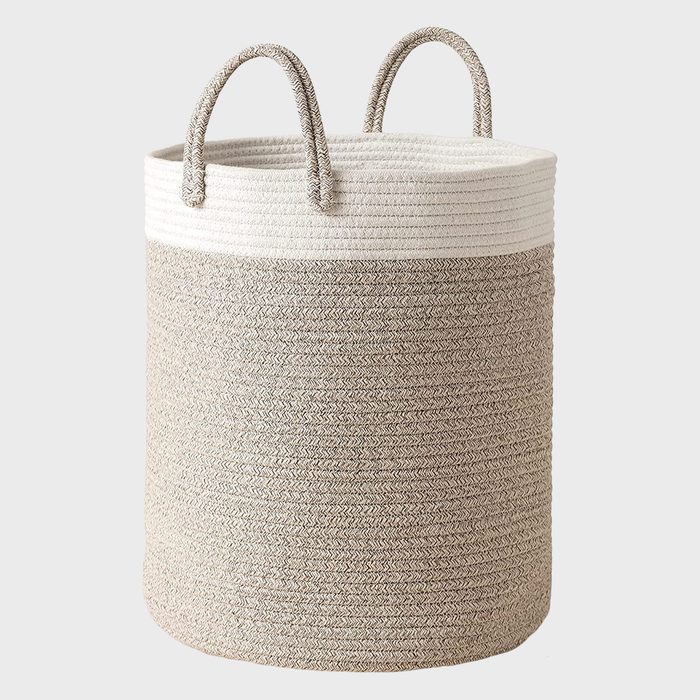 A cylindrical woven storage basket with two handles sits upright, featuring a textured beige and white design, suitable for organizing various items.