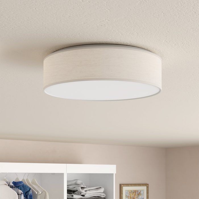 A round ceiling light illuminates a room, hanging above a closet with neatly arranged clothes and a framed picture on the wall.