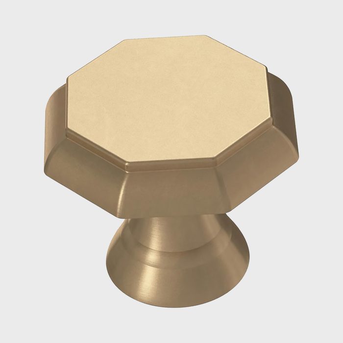 A gold-toned octagonal knob stands upright, showcasing its smooth surface. It is designed for functional use on cabinets or doors.