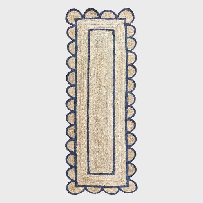 A decorative rug with a scalloped border lies flat, featuring a central rectangular design and contrasting blue outlines against a beige background.
