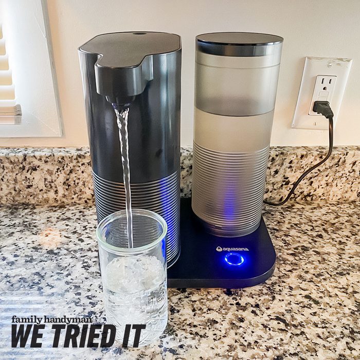 A water dispenser pours water into a glass filled with ice cubes, situated on a granite countertop near an electrical outlet.