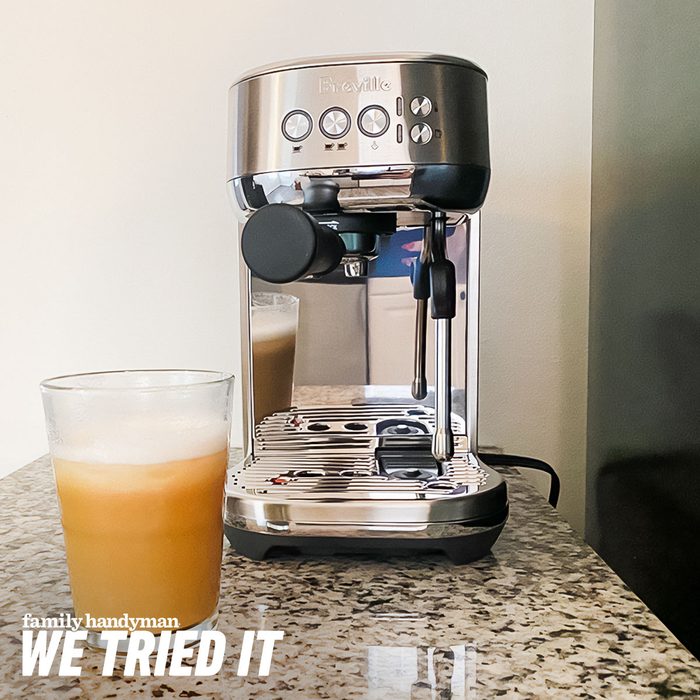 A coffee machine sits on a granite countertop, with a glass of chilled, frothy drink nearby, showcasing its polished design in a bright kitchen setting.