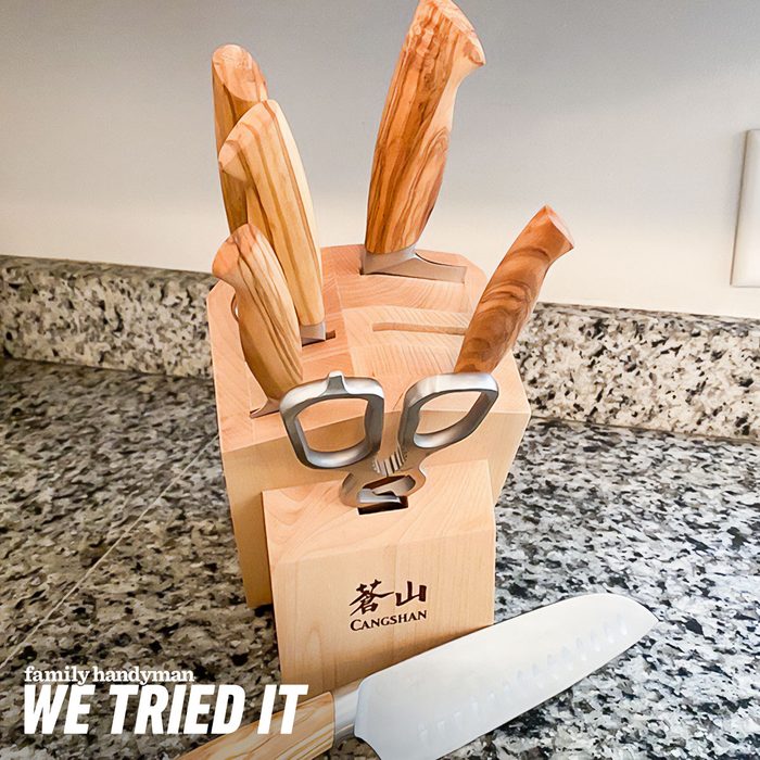 A wooden knife block holds several kitchen knives with wooden handles, alongside a chef's knife on a granite countertop in a brightly lit kitchen.