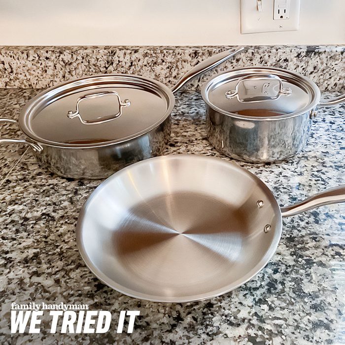 Three stainless steel cookware pieces rest on a speckled granite countertop, with a round frying pan prominently displayed in front of two pots.