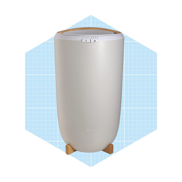 A sleek, cylindrical air purifier stands upright on wooden legs against a light blue grid background, enhancing indoor air quality with modern design.