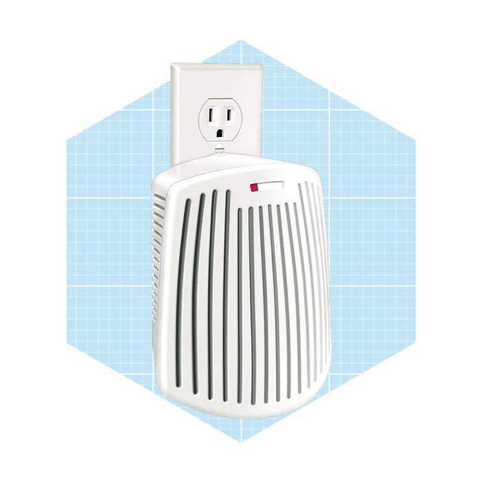 A compact air freshener is plugged into an electrical outlet, actively releasing fragrance in a light blue grid-patterned background.