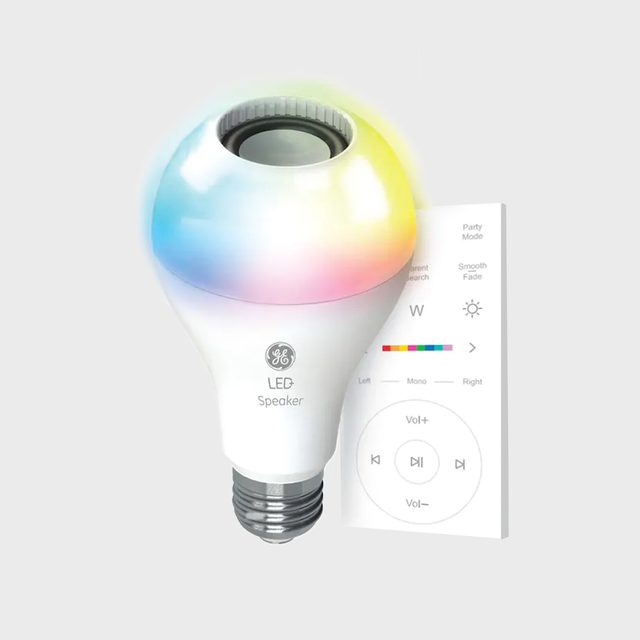 A multifunctional LED light bulb with a speaker emits colorful light, alongside a remote control displaying volume and mode options on a light gray background.